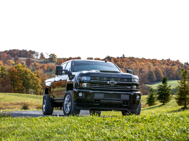 A sleek black Chevrolet Silverado truck parked on a grassy path with a scenic background of rolling hills and autumn trees.